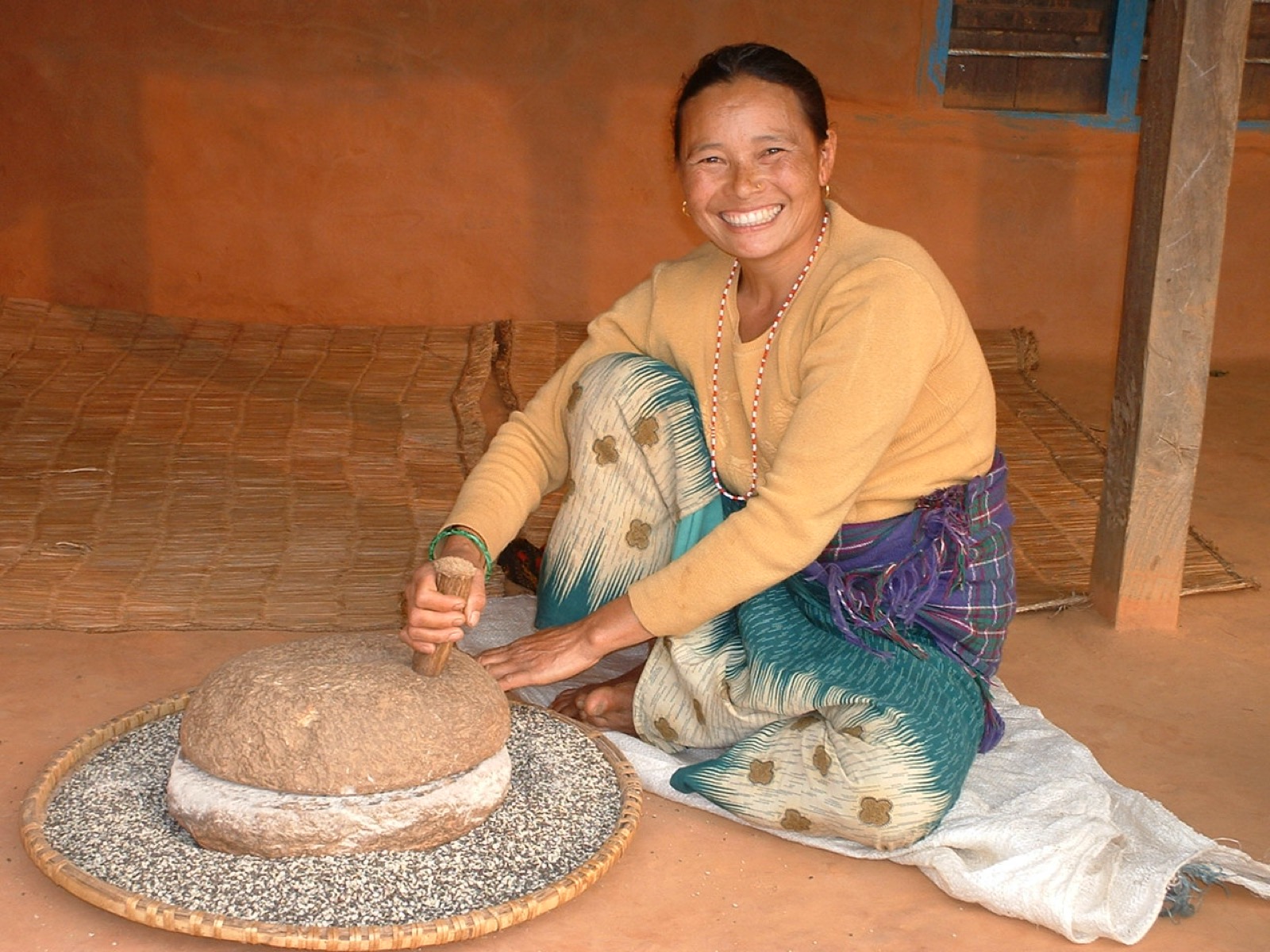 Lady working a grind stone sitting on the floor of a traditional Nepali house